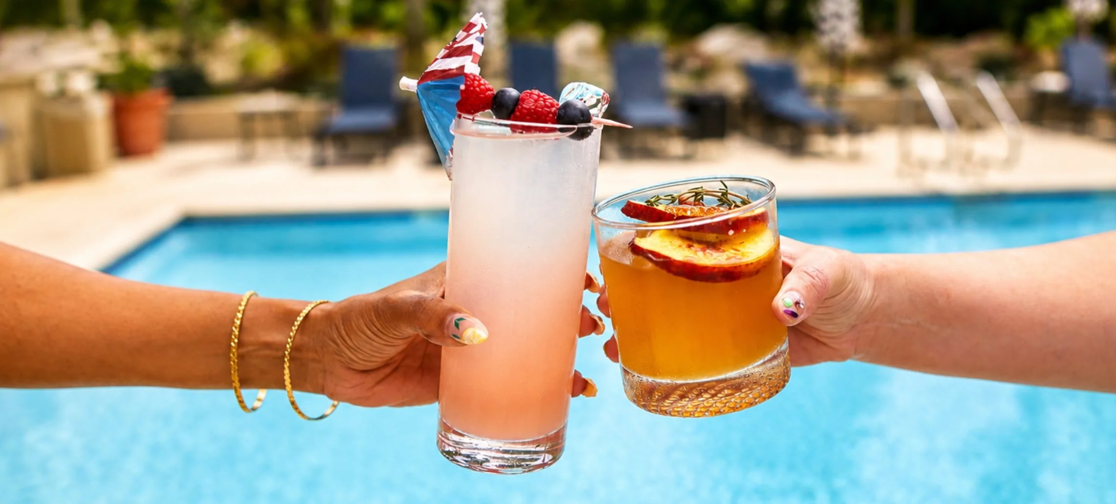 Two people clinking glasses in a cheers over a swimming pool